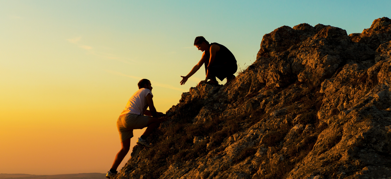 Two people climbing a rocky hillside at sunset.